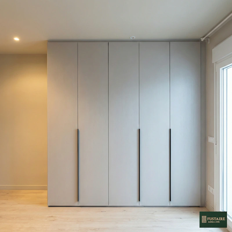 Armario a medida con puertas abatibles en color gris mate y tiradores verticales negros de diseño en dormitorio de Barcelona por Fustaire Mobles a Mida
